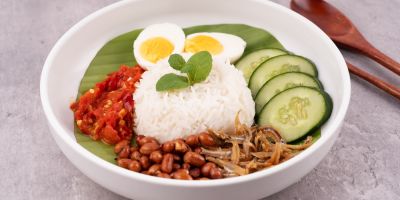 A beautifully plated bowl of Nasi Lemak with rice, eggs, tomatoes, and cucumber.