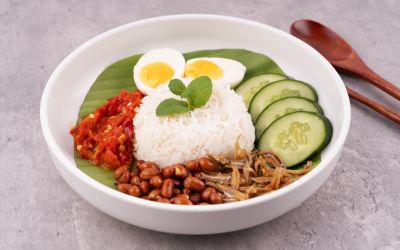 A beautifully plated bowl of Nasi Lemak with rice, eggs, tomatoes, and cucumber.