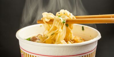 Chopstick holding noodles from a steaming cup of instant ramen