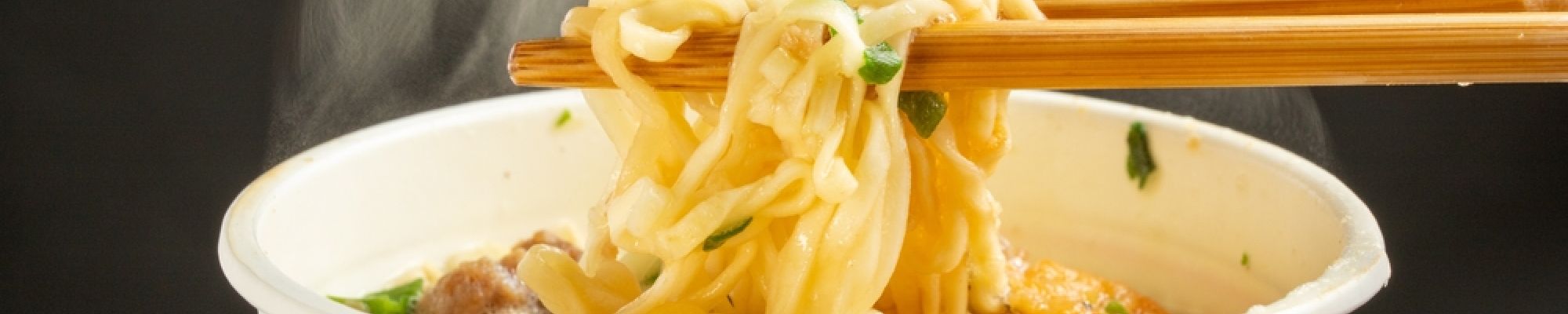 Chopstick holding noodles from a steaming cup of instant ramen