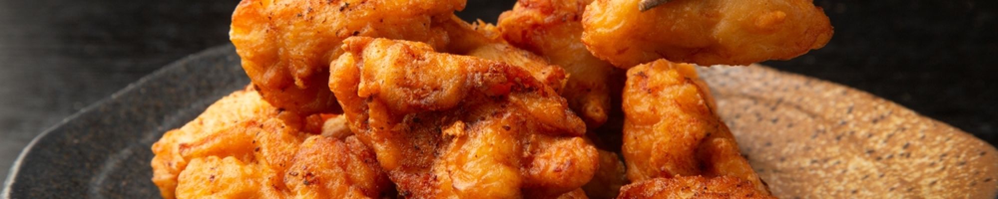 A plate full of chicken karaage being picked up by chopsticks