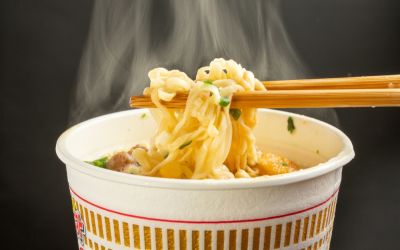 Chopstick holding noodles from a steaming cup of instant ramen