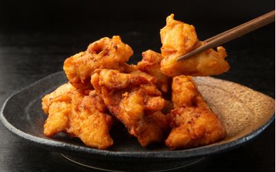 A plate full of chicken karaage being picked up by chopsticks