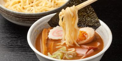 Noodles being dipped into a rich Tsukemen broth with eggs, pork, seaweed, and other various toppings.