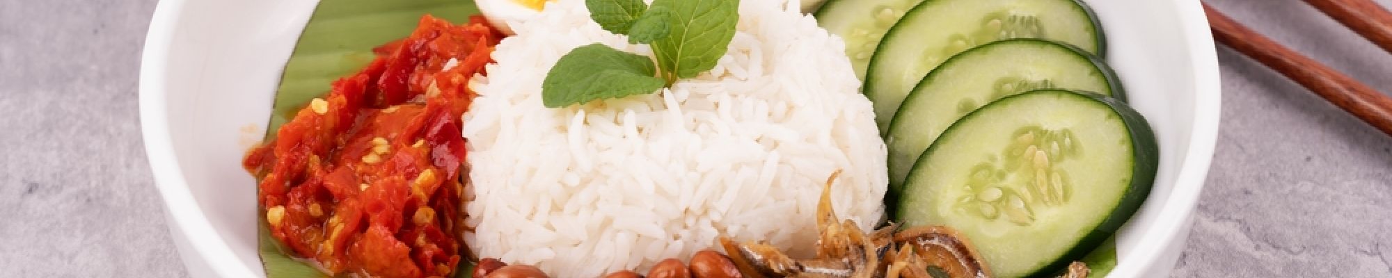 A beautifully plated bowl of Nasi Lemak with rice, eggs, tomatoes, and cucumber.