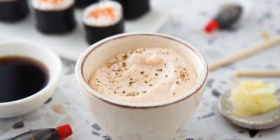 A bowl of seasoned Japanese mayo next to soy sauce, wasabi, and sushi rolls.