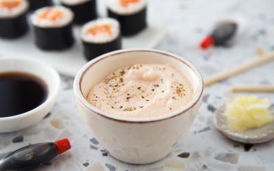 A bowl of seasoned Japanese mayo next to soy sauce, wasabi, and sushi rolls.
