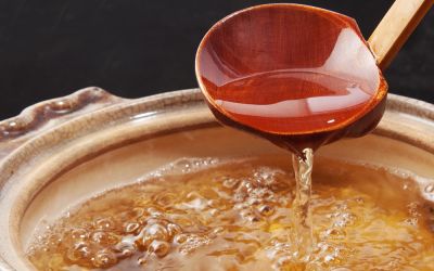 A pot of boiling dashi broth being mixed with a ladle