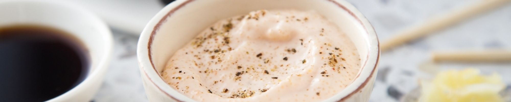 A bowl of seasoned Japanese mayo next to soy sauce, wasabi, and sushi rolls.